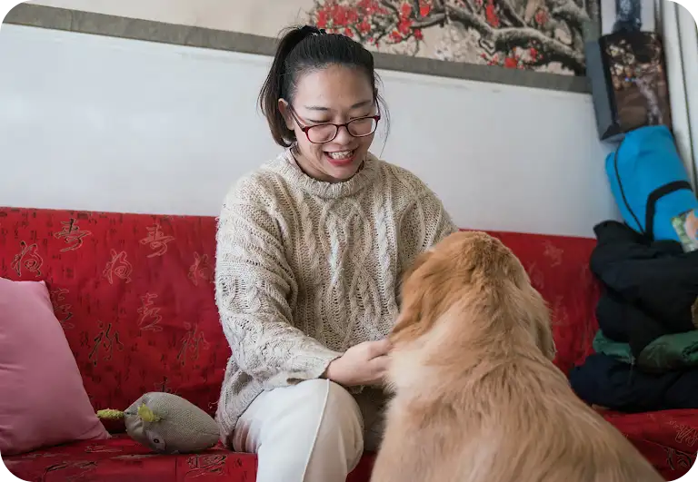 A woman is seated on a couch petting an off-duty guide dog